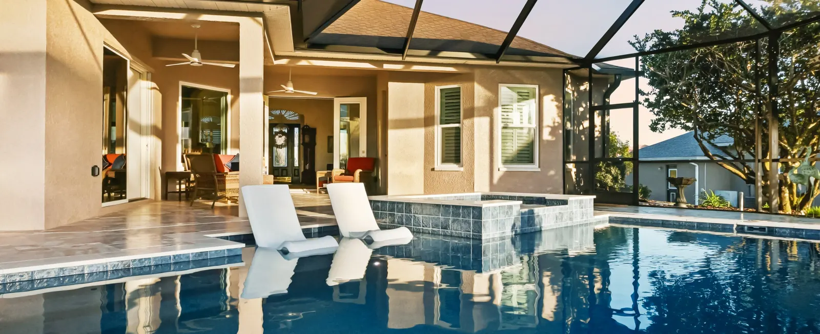 Screened lanai pool and spa with lounge chairs overlooking a golf course at dusk.