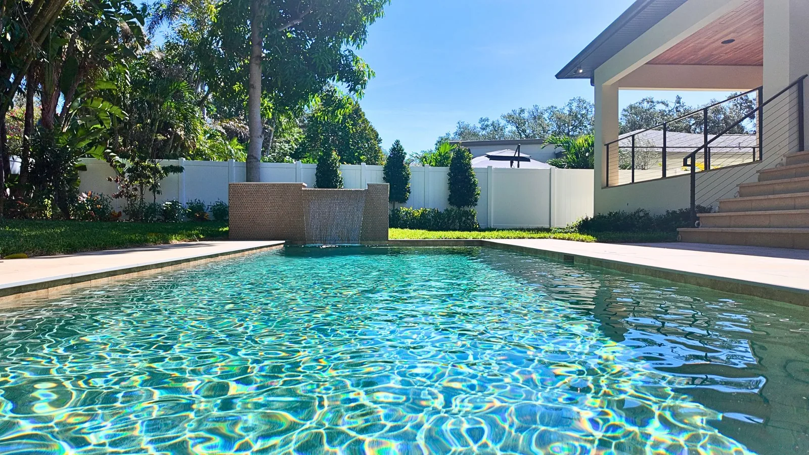 Sunlight breaking across the length of the pool, the covered porch and its cable railing at the far corner.
